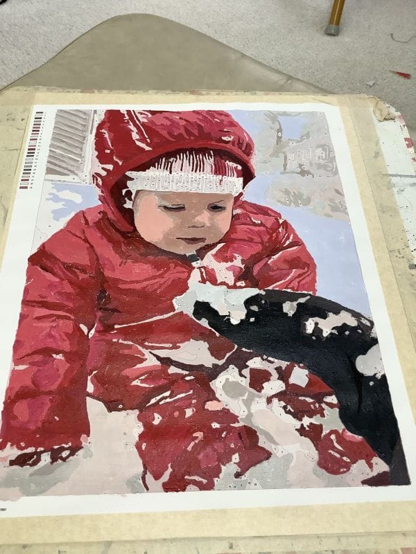 Almost completed custom paint by numbers kit of a baby in red jacket.